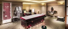 Tiled treatment room with a bed surrounded by candles, a hanging robe, small bathtub, shower and shelf with a Buddha statue and sound bowls underneath 