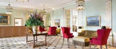 Elegant reception area with red velvet armchairs, a chequered floor, table with large flower arrangement, and wooden desk with chandelier-style lighting