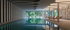 Indoor pool area with wooden loungers, mood lighting and full-length windows with a view of tropical greenery outside