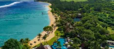 Aerial view of a tropical resort, with palm trees, a golden beach, thatched umbrellas and swimming pools