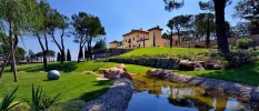 Italian villa with a terracotta roof and green window shutters overlooked manicured grounds and a stream