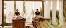 Two massage therapists working on clients in an airy outdoor massage cabin, with white curtains keeping things private
