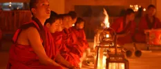Monks in red robes sitting among lanterns and a fireplace