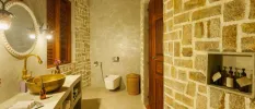 Rustic bathroom with stone walls, a wooden door and window, and a vanity unit with a large gold sink and mirror