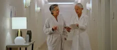 Woman in a white robe walking down a corridor with a healthcare professional in a white jacket holding a booklet open