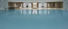 Indoor swimming pool surrounded by marble and wooden walls and with spotlights in the white ceiling