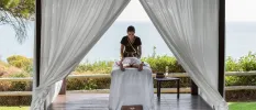 Woman lies on her front in an open-air white cabana in front of the ocean, while enjoying an outdoor massage