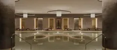 Chic indoor pool area with grey marble-like walls and pillars, contemporary pendant lights, and LED lighting with vases lined along the back wall