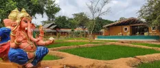 Hindu elephant statue in a leafy courtyard, with a thatched-roof pavilion in the background