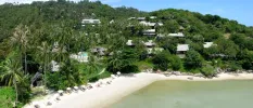 Tropical green hillside with a white-sand beach and pale blue waves under a blue sky