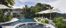 Swimming pool and whirlpool bath surrounded by tropical greenery and parasols