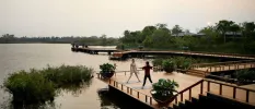 Two women in active wear stand on a wooden deck on a riverfront surrounded by greenery