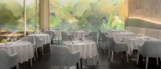 Restaurant with grey chairs and white tablecloths, with a colourful abstract wall mural behind