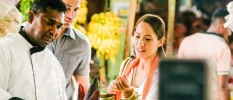 Chef in whites preparing ingredients as two guests watch on smiling