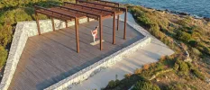 Man on a wooden deck practicing yoga overlooking the ocean and surrounding greenery