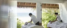 Two people enjoy a massage on neighbouring beds in an open-sided cabana with a view of the ocean