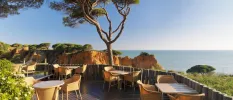 Al fresco terrace with wooden tables and chairs and a view of the surrounding cliffs, greenery and ocean