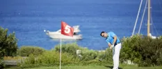 Man swings a golf club on greens in front of the sea