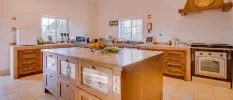 Spacious kitchen with a wooden island and surrounding units, white walls and a bowl of fruit at the centre