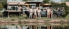 Game drive professionals pose in camo attire outside a lodge with a safari vehicle