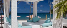 Four-poster seating area with white curtains, white sofas and blue cushions on the beach 