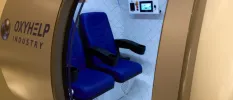 Door open on an oxygen chamber with two blue chairs and a side panel