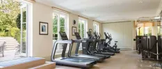 Treadmills and step machines lined up in an airy gym, with doors opening onto a furnished sunny terrace