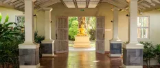 Entranceway with terracotta floor tiles, white pillars, potted plants and a gold Buddha statue
