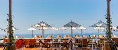 Wooden terrace with tables and chairs, white parasols and a view of the sea in the background