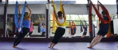 Group in active wear hang from ribbon harnesses opposite a mirror in a fitness class
