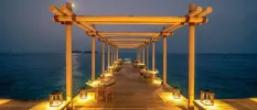 Wooden lantern-lit jetty laid out with tables and chairs as the sky darkens