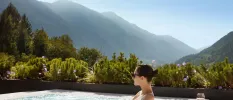 Woman in sunglasses relaxing in an outdoor pool overlooking flowers, trees and mountain peaks in the sunshine