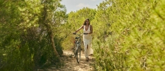 Woman in white steers a bicycle down a rural path surrounded by greenery