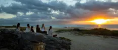 Group sitting on rocks on the beachfront, watching the sun rise or set above the ocean