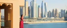 Woman in a pink dress gazes out at the Dubai skyline and sea from a glass-fronted balcony