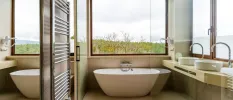 Modern bathroom with neutral vanity unit, walls and a white bathtub with a large window overlooking the countryside