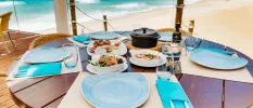 Round wooden table on the beachfront with blue plates and napkins and white plates of seafood and salad