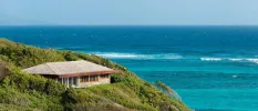 A building nestled among greenery on a hillside overlooking the ocean