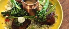 Yellow plate piled with vegetables and grains including tender stem broccoli, with a small jug of dressing at its centre
