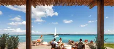 Thatched-roof pavilion framing a view of people sitting on chairs and beanbags on a waterfront deck under a blue sky