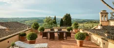 Concrete patio rooftop above tiled roofs, with terracotta potted plants and a view of the surrounding countryside