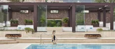 Woman in a black swimsuit walking into an outdoor pool with mountain peaks in the background