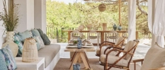 Boho-style accommodation terrace with white and blue soft furnishings, wooden furniture and rattan lanterns overlooking a forest