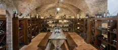 Medieval stone wine cellar with chunky wooden benches, a stone table and shelves stacked with bottles