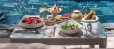 Tray of nutritious, colourful food laid out on a poolside, including a green salad, edible flowers, and fresh fruit