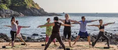 Group practice yoga on the shoreline with the waves and green hillsides in the background