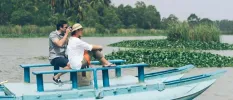 Man and woman enjoying the view of surrounding water and tropical greenery in a wooden boat