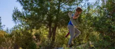 Woman in active wear walking up a hill among greenery under a blue sky