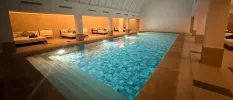 Indoor swimming pool with underwater lighting, surrounded by white daybeds