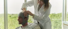 Man sitting in a chair with an apparatus on his head as a health expert fixes it on